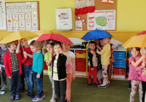 Dzieci spacerują pod żółtymi, czerwonymi i niebieskimi parasolami